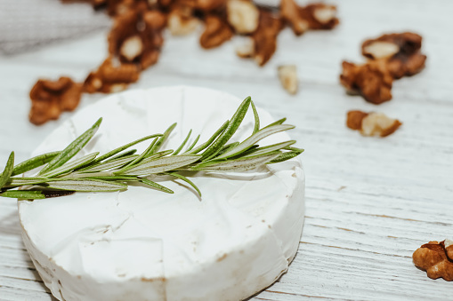 Round cheese in camembert mold with a sprig of rosemary on the table.