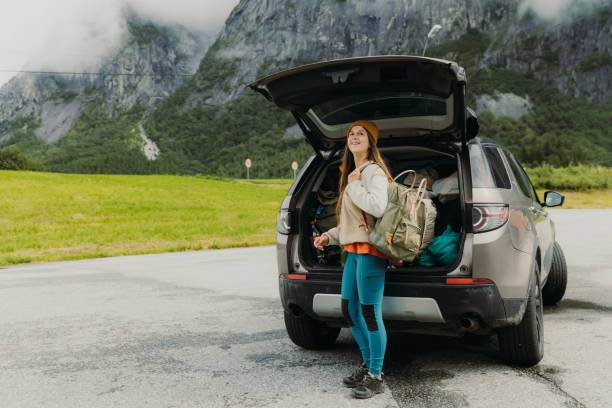 Happy woman traveler packing backpack in the car during road trip in Norway stock photo