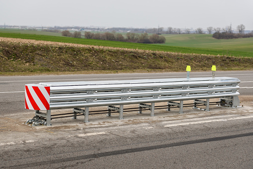 Installation of median crash barriers on highway. Metal road fencing of barrier type on freeway. Road guard rails. Safety barrier with a red and white striped sign. Protect vehicles from accidents.