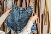 Woman choosing  summer denim shorts  from assortment of female modern summer and autumn clothing in garment store. Shopping.