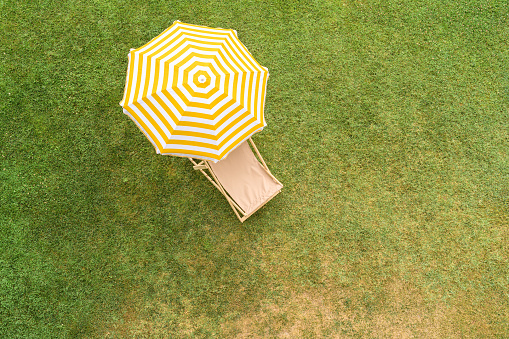 Yellow umbrella with deck chair on the green grass sunbathes at summer day. Top view, drone, aerial view.