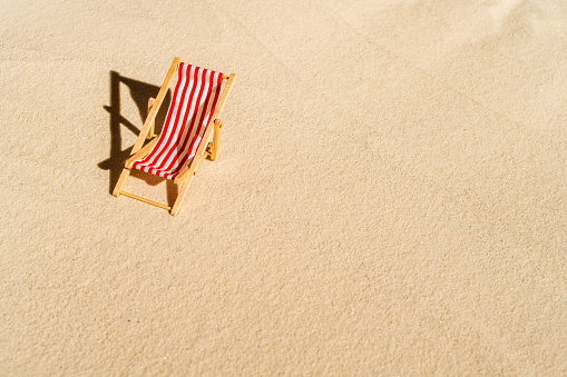 Aerial view of one deck chair, sunbed, lounge, glass of orange juice, flip flops, Lifebuoy, palm tree on sandy beach. Summer and travel concept. Minimalism