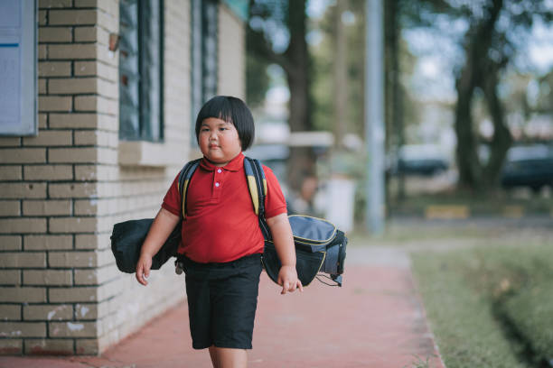 Asian Chinese young boy walking to golf driving range with golf bag for lesson practising
