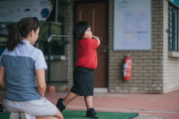 Asian Chinese young boy practicing golf at driving range guided by female instructor