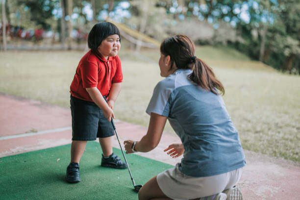 azjatycki chiński chłopiec robiący twarz instruktorowi golfa ćwiczy zajęcia na strzelnicy - golf child sport humor zdjęcia i obrazy z banku zdjęć