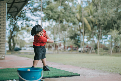 Asian Chinese cute boy practicing gold swing in driving range during golf class