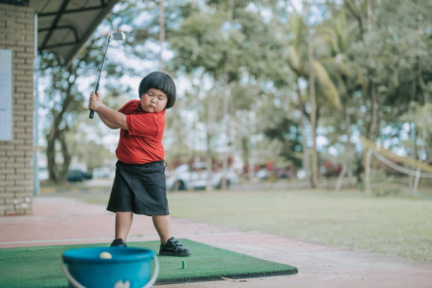 азиатский китайский симпатичный мальчик практикует золотой свинг на тренировочном поле во время урока гольфа - golf driving range practicing bucket стоковые фото и изображения
