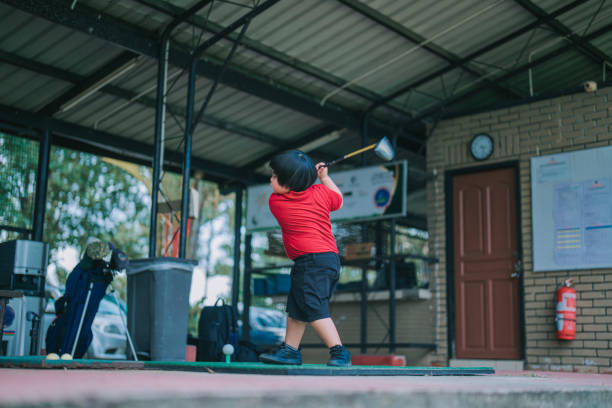 азиатский китайский симпатичный мальчик практикует золотой свинг на тренировочном поле во время урока гольфа - golf driving range practicing bucket стоковые фото и изображения