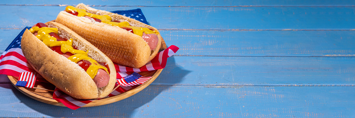 USA Patriotic picnic holiday hot dogs.  American patriotic hot dog on wooden board plate, with USA flag. Celebrating Independence day on 4th July, Memorial or Veteran Day