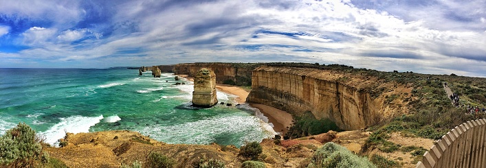 This mesmerizing image captures the awe-inspiring 12 Apostles beach, located in Melbourne, Australia. The picture-perfect beach boasts crystal-clear, emerald-green waters that elegantly break against the rugged and towering rocky mountains that surround it. The partially cloudy sky sets the perfect backdrop for the breathtaking view, evoking a sense of calmness and tranquility.\n\nThis image is ideal for a wide range of uses, including travel brochures, promotional materials for the tourism industry, and even as a centerpiece for nature and landscape enthusiasts' home or office décor. The image can also be used as a desktop wallpaper for those who want to be reminded of the beauty of nature and the wonders of the world. Whatever the use, this captivating image is sure to leave a lasting impression and inspire viewers to explore the natural beauty of Melbourne's 12 Apostles beach.