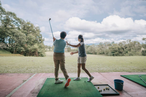 китаянка азиатского происхождения учится руководить свингом в гольфе у женщины-тренера на тренировочном поле - golf driving range practicing bucket стоковые фото и изображения