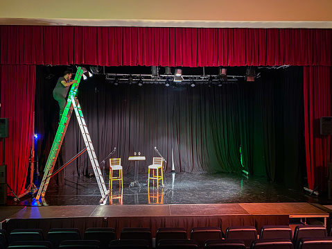 Young male light technician standing on a ladder installing spotlights on a theater stage