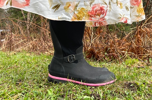 Partial lower view of a teenagers rubber boots and flowered dress. Only a small part of her dress can be seen, she is lifting it above her boots, standing in her emerging spring yard. Taken in a rural yard in Northern Wisconsin with grass and plants surrounding the teen.