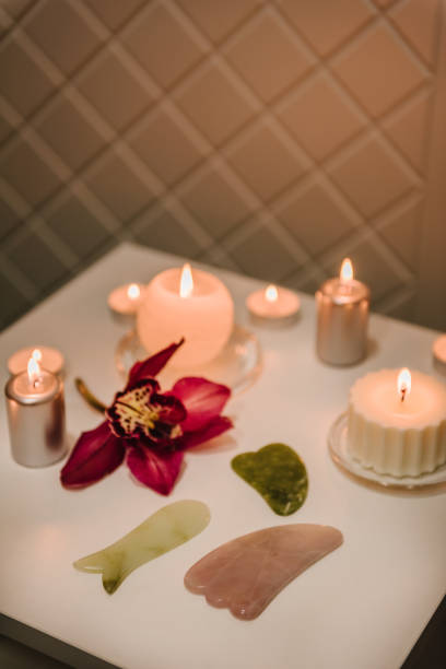 Gua sha tool. Сandles, and orchid flowers on table. Facial massage for lifting, face therapy, home spa, mockup. Skincare concept. Cosmetology, body massage, spa procedure. Details decor in spa salon. herramienta gua sha. Сandles, y flores de orquídeas sobre mesa. masaje facial para lifting, terapia facial, spa casero, maqueta. concepto de cuidado de la piel. cosmetología, masaje corporal, procedimiento de spa. detalles de decoración en salón spa