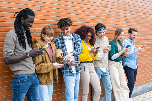 Young people looking down at cellular phone, teenagers leaning on a wall and texting with their smartphones, concepts about technology and communication