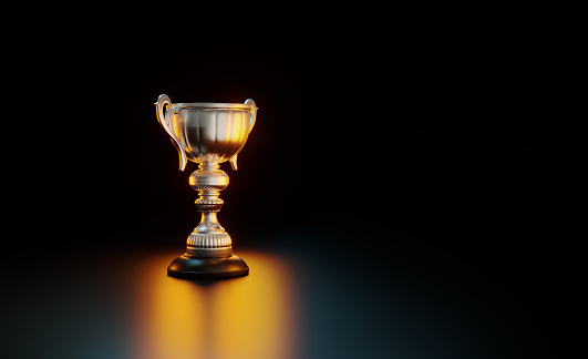 Silver colored trophy illuminated by yellow and blue lights on black background. Horizontal composition with copy space. Award concept.