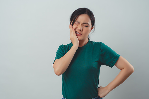 Asian woman was sick with toothache touching her cheek and standing isolated on background.