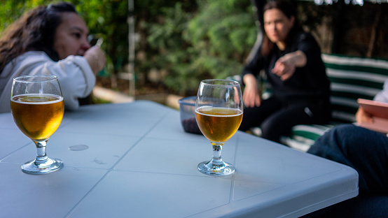 two beer glass are on white table on foreground focus on foreground two women are background outdoor activities horizontall still