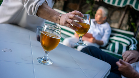 women hand is taken beer glass on table focus on foreground mature women is background at garden horizontal family activities still