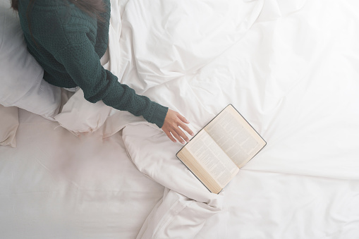Pretty smiling young asian woman relaxing at home on bed and reading book. Lifestyle concept.