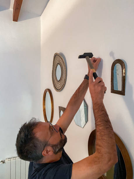 istock Man with a hammer hammering nails into the wall to hang mirrors 1486837393