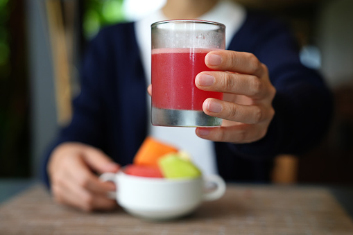 Cropped shot of a young Asian woman enjoying a a refreshing watermelon juice along with  tropical papaya fruit in a bowl. The image represents the concept of healthy eating and detox diets.