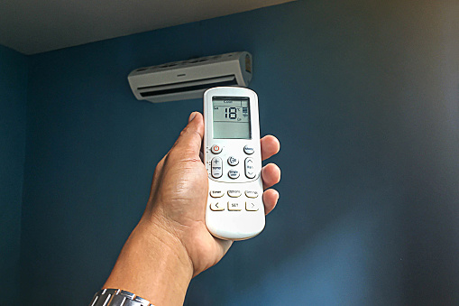 Adjusting the temperature of the air conditioner in the room. Air conditioner with remote control.