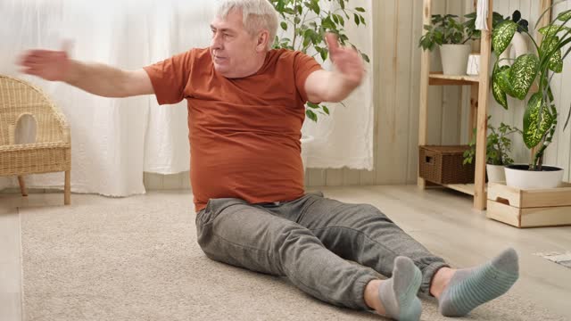 Happy smiling mature senior man doing exercises of gymnastics at home. Concept of healthy lifestyle, fitness, recreation, well being. Elderly male exercising training, stretching. Old man working out.