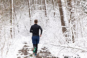 The young man is running on a forest road during winter.