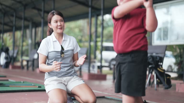 Asian Chinese female coach guiding young boy in driving range golf lesson holding golf club