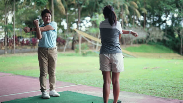 Asian Chinese woman stretching warm up exercise at golf driving range with instructor before practicing