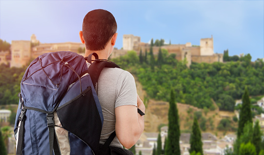 Traveler boy in europe and looking at the Alhambra in Spain with backpack and back