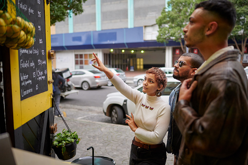 Group of diverse young friends standing outside together on a city street and looking at a restaurant menu