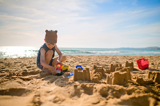 Girl playing on a sandy beach on summer vacation. A child is building a sand castle on the sea.