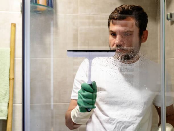 istock Cleaning services, man cleans glass wall in bathroom using wiper for glass. 1486858171
