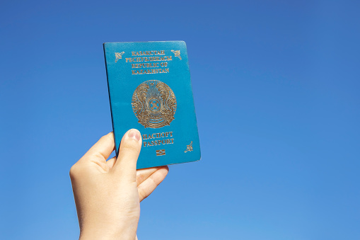 Hand holds the national passport of the Republic of Kazakhstan against the blue sky background. High quality photo