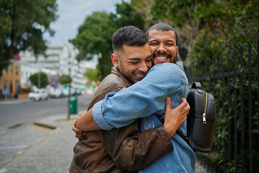 Smiling young gay couple hugging with their eyes closed while standing together outside in the city
