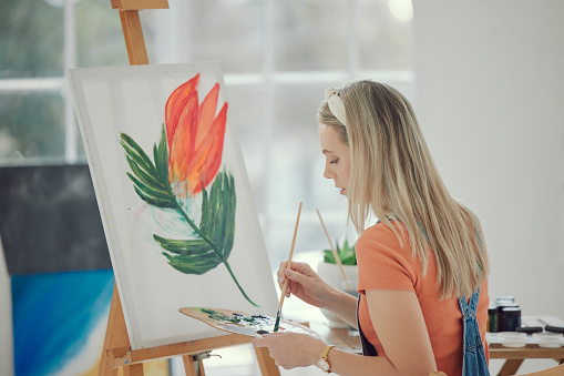 Paint, flower and color pallet with a woman in a studio or workshop painting on a canvas using an easel and oil paint. Watercolor, inspiration and art with a young female painter sitting in her home