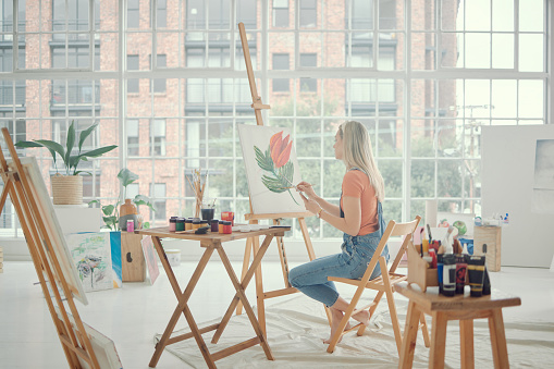 Painting, art or flower with a woman in a workshop or studio for creative artwork on a canvas using an easel and oil paint. Watercolor, inspiration or artistic with a young female painter in her home