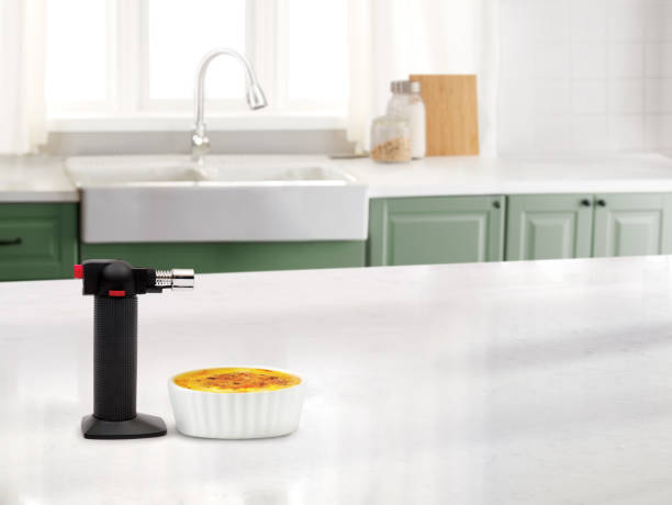 Creme Brulee in a cup with a small portable torch in a kitchen.