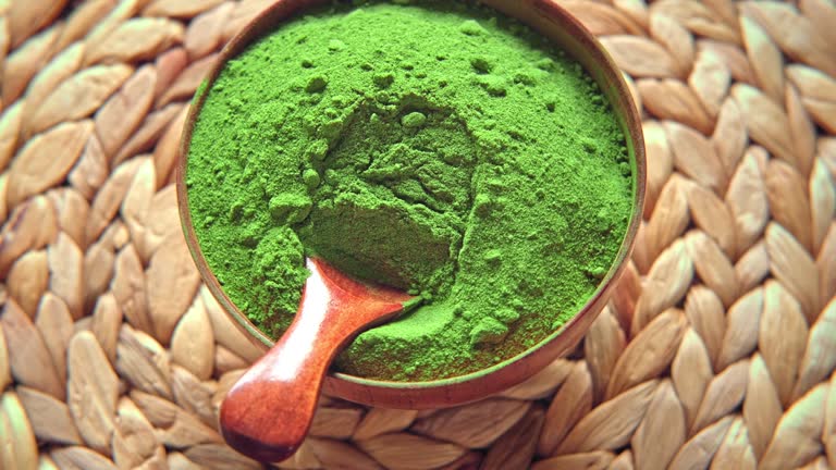 Wooden spoon with powdered matcha tea in a bowl spinning on natural background. Matcha powder. Top view, Closeup. Finely ground green powder. Japanese culture. Healthy eating with high antioxidants