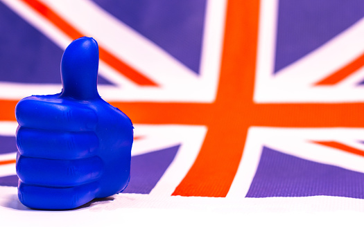 A blue thumb giving approval in front of a British flag.