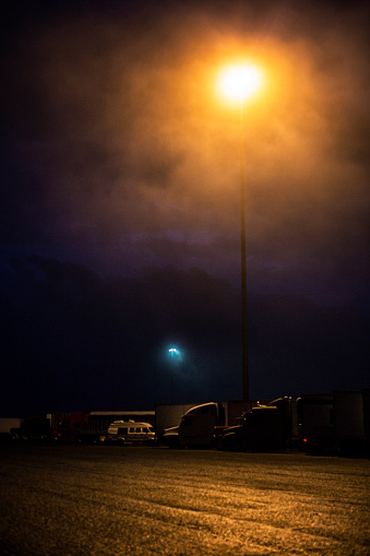 Very tall high pressure sodium vapor street light during a stormy overcast night at an interstate expressway trailer truck rest stop.