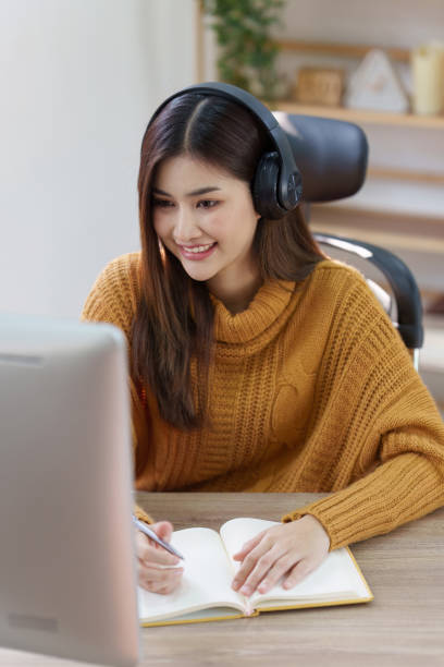 istock Online education, e-learning. Asian woman in stylish casual clothes, studying using a computer, listening to online lecture, taking notes, online study at home 1486882980