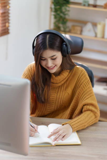 istock Online education, e-learning. Asian woman in stylish casual clothes, studying using a computer, listening to online lecture, taking notes, online study at home 1486883023