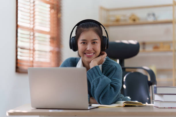 istock Online education, e-learning. Asian woman in stylish casual clothes, studying using a laptop, listening to online lecture, taking notes, online study at home 1486886148