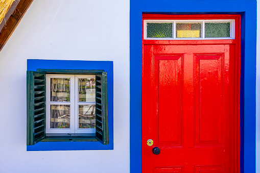 detail of a small window with a blue frame and a red door in a traditional and typical house in the parish of Santana, Madeira Island.