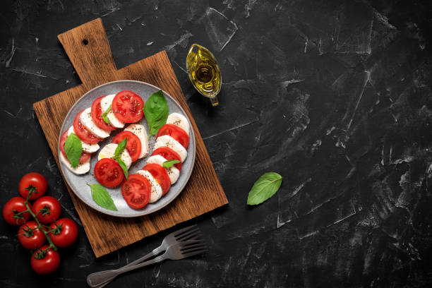 italian caprese salad with chopped tomatoes, mozzarella, basil, olive oil on a black stone background. top view, flat lay - caprese salad salad restaurant vinegar imagens e fotografias de stock