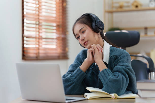 istock Online education, e-learning. Asian woman relaxing after studying using a laptop, listening to online lecture, taking notes, online study at home 1486890022