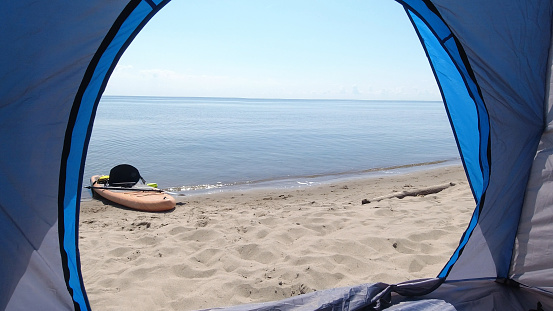Tranquil and relaxing views from the travel tent on the beach and puddle board SUP during summer vacation holidays. Sandy beach and waves crashing with sun leaks and light reflection.